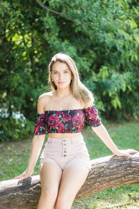 Portrait of teenage girl sitting on tree trunk against plants in park