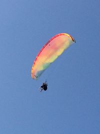 Low angle view of people paragliding against clear blue sky