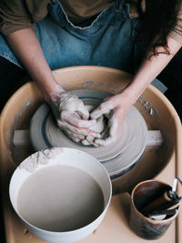 Unrecognisable ceramist sitting on bench with pottery wheel and making clay pot