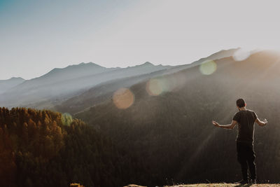 Rear view of man standing on mountain against sky