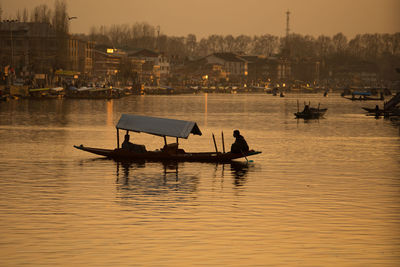 Silhouette people on boat sailing in river against sky during sunset