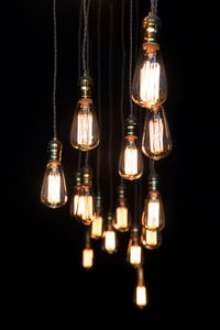 Close-up of illuminated light bulb hanging against black background