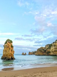 Scenic view of sea and rocks against cloudy sky