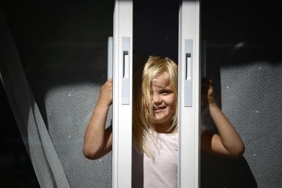 Portrait of smiling girl looking through window during sunny day