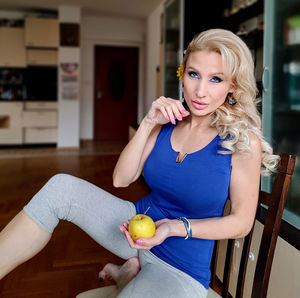 Portrait of mature woman with apple sitting on chair at home