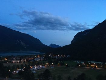 Illuminated city by mountains against sky at night