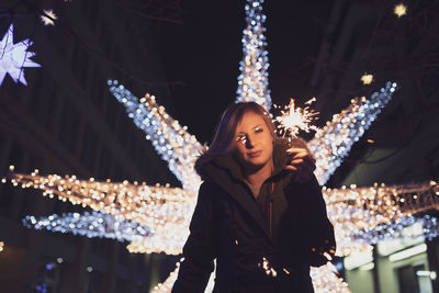 Portrait of woman holding illuminated sparkler at night