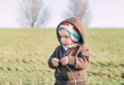 Cute girl in warm clothing standing on field