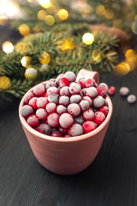 Close up of cup with fresh frozen cranberries on dark rustic background with christmas lights