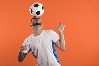 Rear view of man playing soccer while standing against yellow background