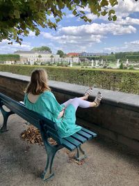 Girl sitting on bench against sky