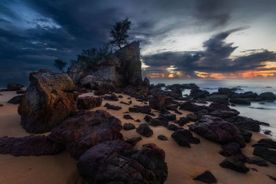 Rocks on beach against sky during sunset