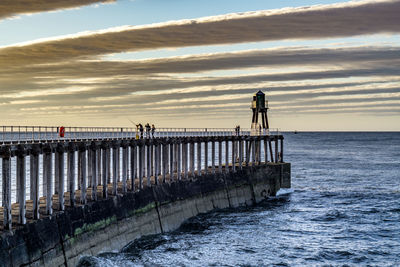Men standing on pier by sea against sky during sunset