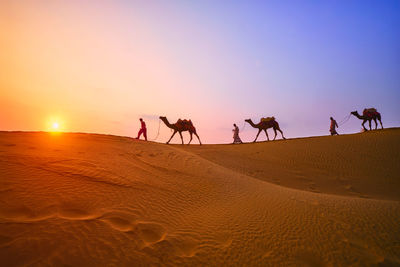 People on sand dune in desert against sky