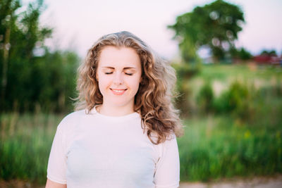 Smiling young woman with eyes closed standing outdoors