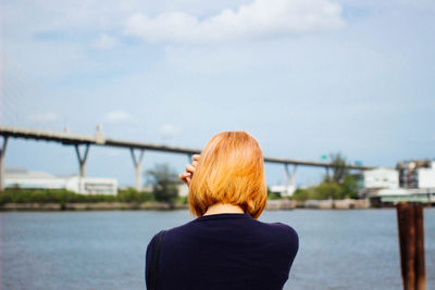 Rear view of woman by river against sky