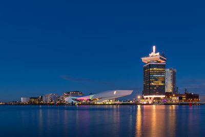 Illuminated buildings in city by sea against sky at night