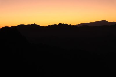 Scenic view of silhouette mountains against orange sky