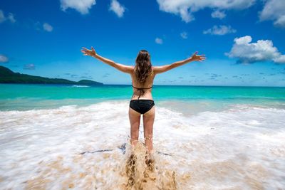 Rear view of woman standing at beach against sky