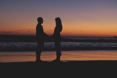 Silhouette couple standing at beach during sunset