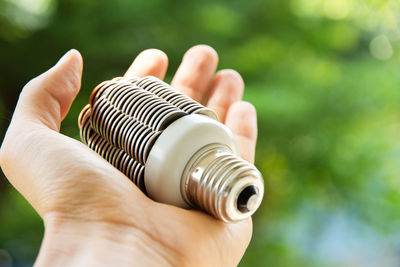 Cropped hand of man holding light bulb against plants