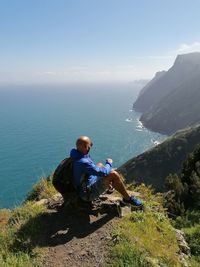Man sitting on mountain by sea against sky