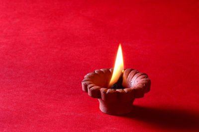 Close-up of lit candle against red background