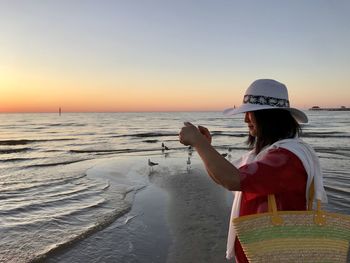 Side view of woman at beach against sky during sunset