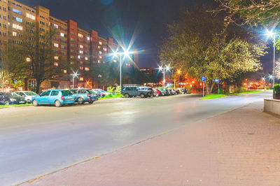 Illuminated street by buildings in city at night