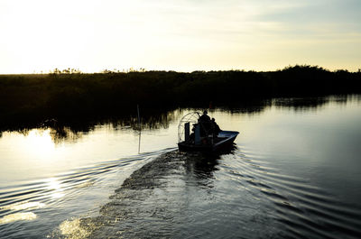 Men on boat in lake against sky during sunset