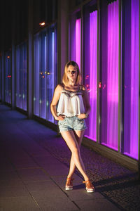 Young woman standing by illuminated windows at night
