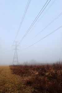 Electricity pylon on field against sky during foggy weather