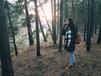 Full length of young woman having drink while standing in forest