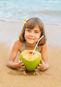 Portrait of smiling girl with coconut lying on beach