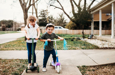 Young brother and sister riding scooters in front yard