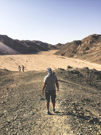 Rear view of man standing on ground against clear sky at desert during sunny day