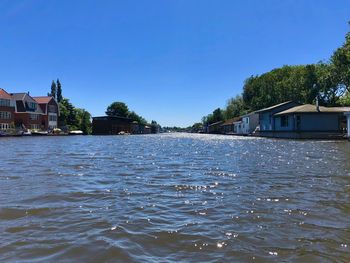 Scenic view of river by building against clear blue sky