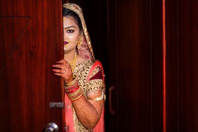 Portrait of woman in traditional clothing hiding behind door at home