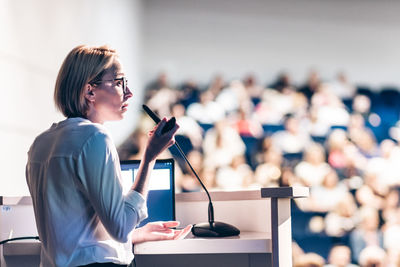 Female speaker giving a talk on corporate business conference. unrecognizable people in audience at