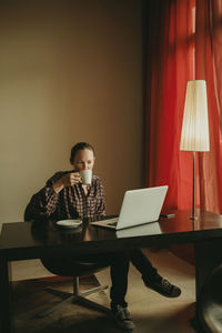 Businesswoman drinking coffee while working on laptop in office