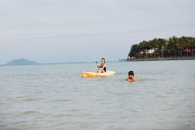 People kayaking in sea against sky