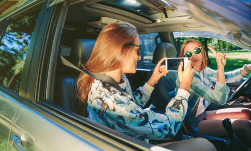 Woman photographing friends with mobile phone in car