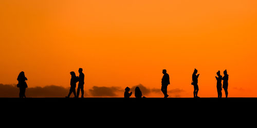 Silhouette people standing against orange sky