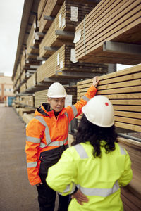 Mature female worker discussing with colleague while standing by stack of planks