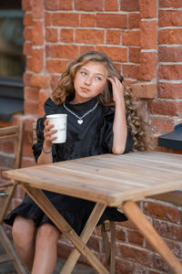 Portrait of young woman sitting on chair against brick wall