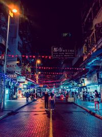 People walking on illuminated street amidst buildings at night