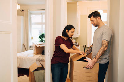 Woman unpacking box held by man in corridor at new home