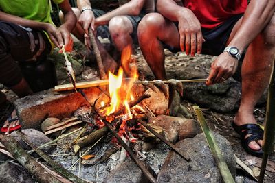 Low section of friends preparing fish on campfire