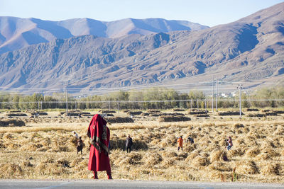 Rear view of people walking on field against mountain range