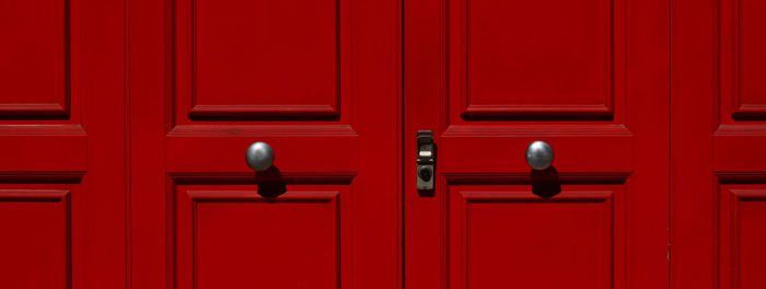 Portion of door in red lacquered wood with metal knobs and lock.